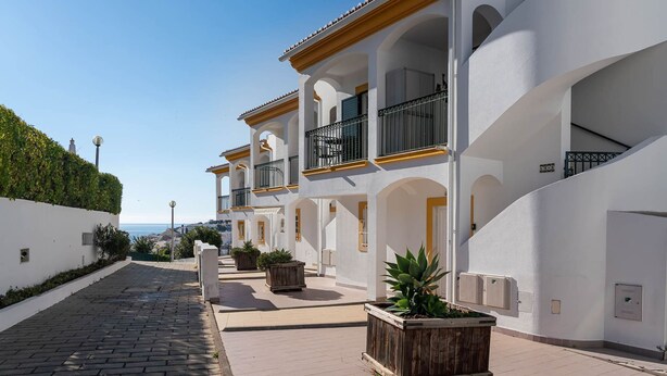 A row of white buildings with balconies, a paved walkway, and potted plants. - Lily Fabulous 1 BED APT With Roof Terrace Pool (Lagoa)
