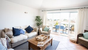Un salón con sofá, sillón, mesa de centro y vistas al exterior.