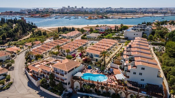 Zona residencial costera con casas escalonadas, una piscina central y un puerto deportivo al fondo.