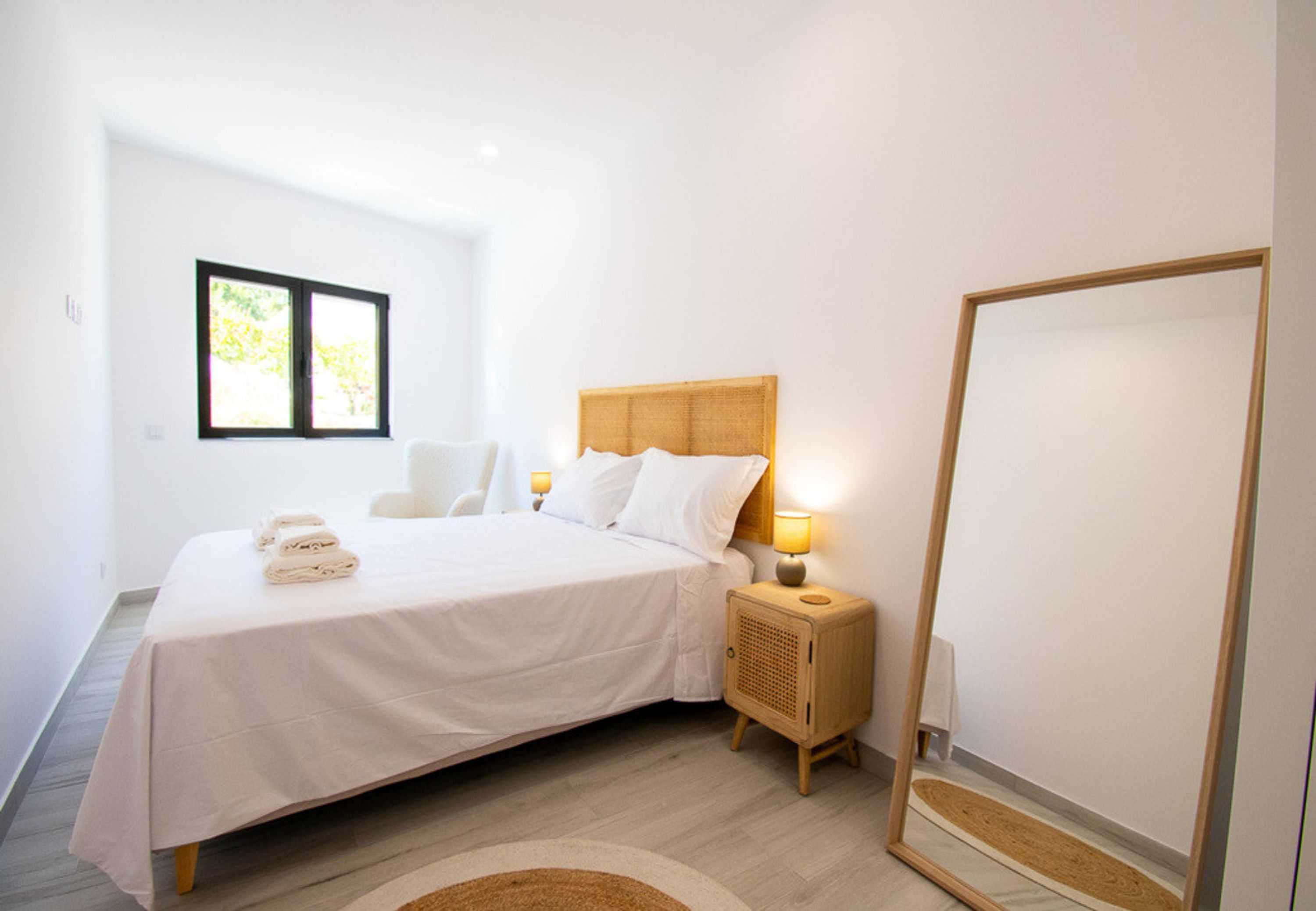 Une chambre moderne avec un grand lit, des lampes de chevet, un miroir et une fenêtre donnant sur la forêt.