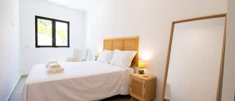 Une chambre moderne avec un grand lit, des lampes de chevet, un miroir et une fenêtre donnant sur la forêt.