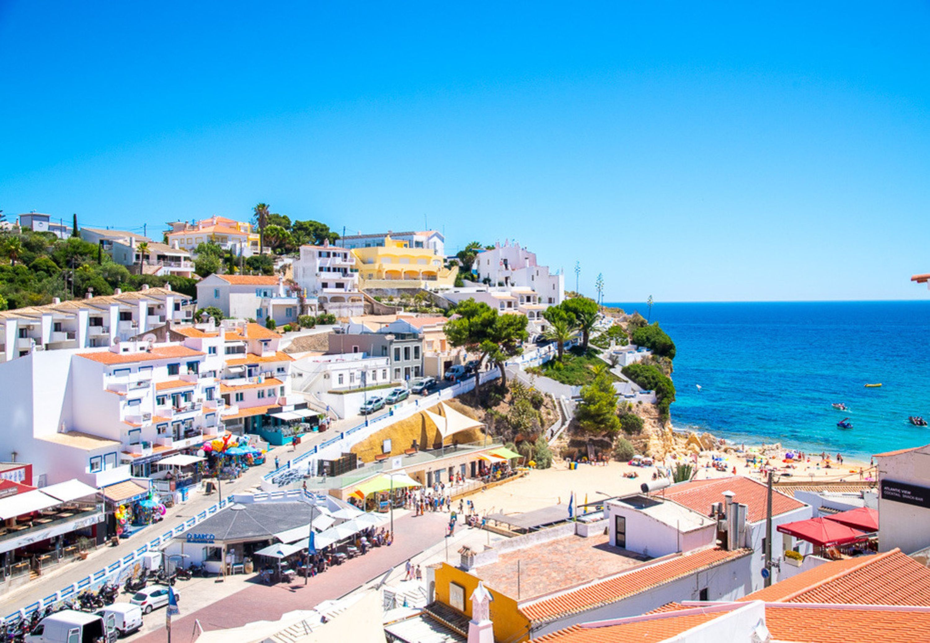 A coastal town with buildings along the waterfront, a beach, and a clear blue sky.
