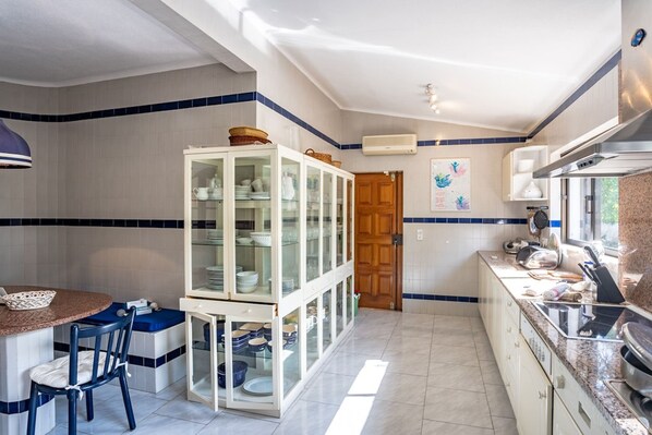 A kitchen with a dining area, featuring a cabinet with glass doors, a stove, and a window.