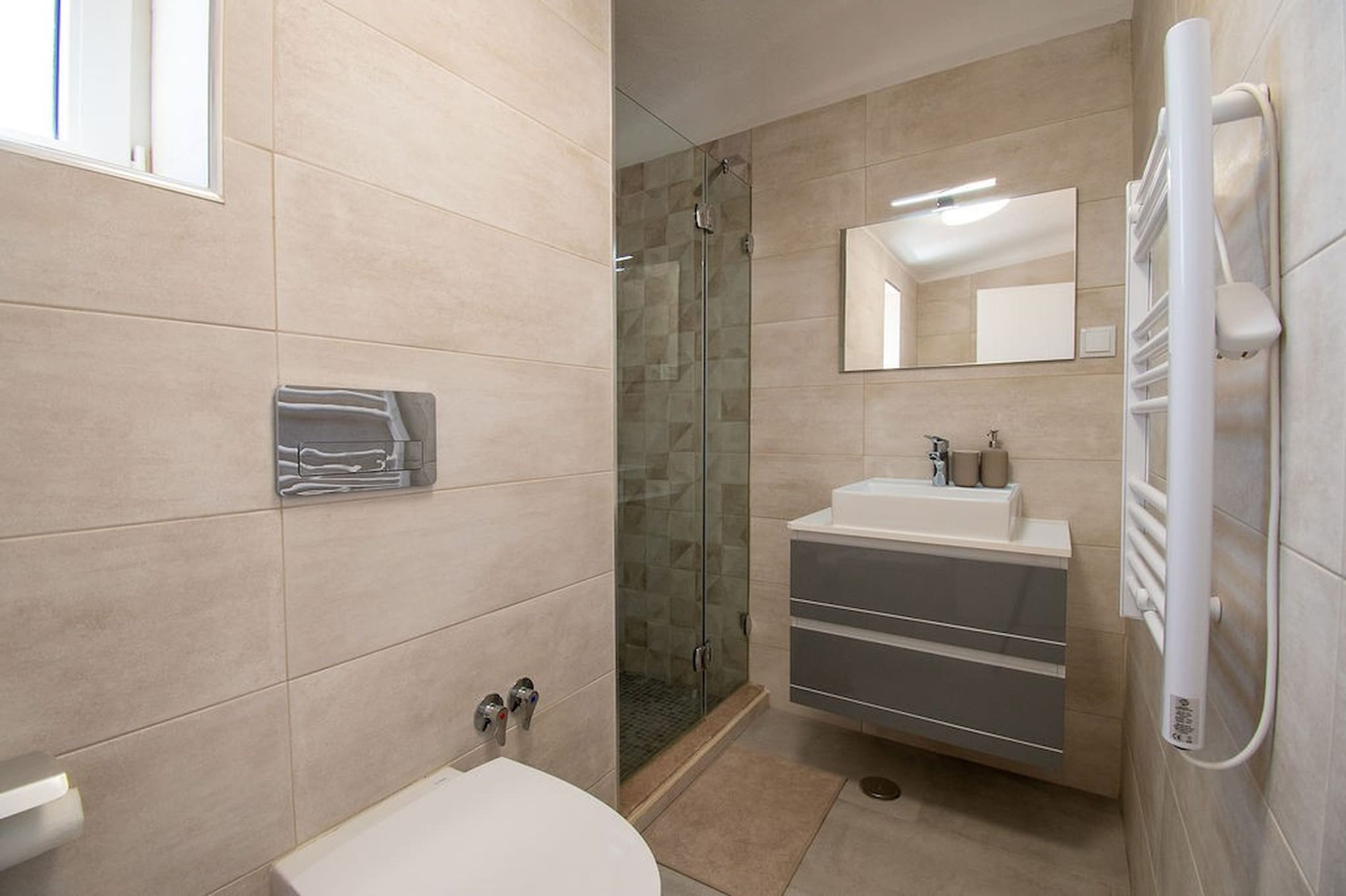A modern bathroom with a glass shower enclosure, a white sink, and a built-in towel rack.