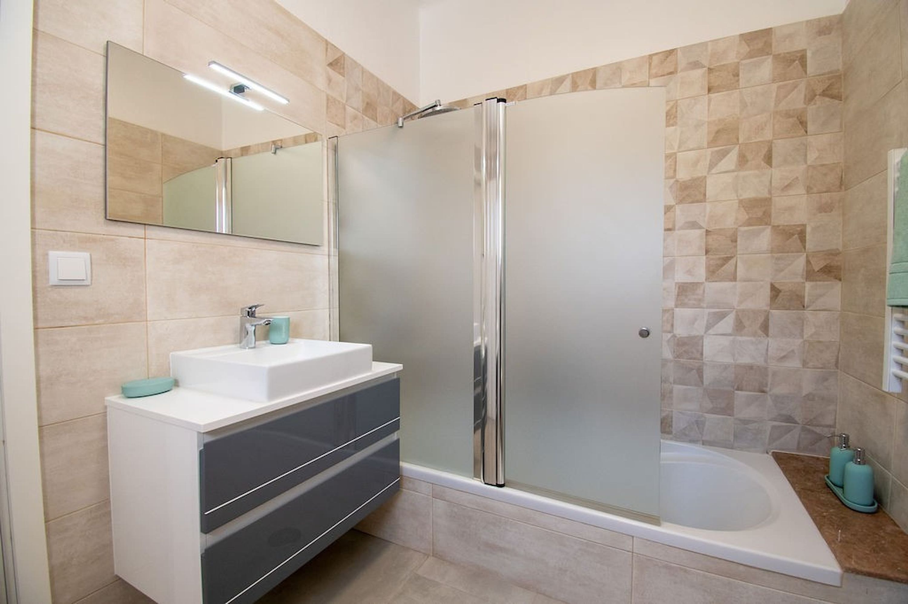 A modern bathroom with a glass-enclosed shower, a white sink with a mirror, and a bathtub.