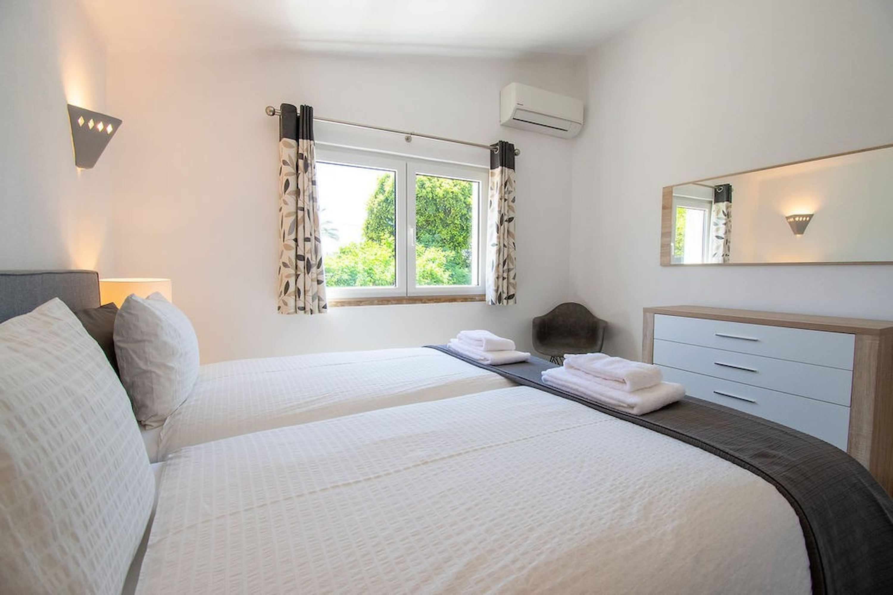 Une chambre d’hôtel avec deux lits, une table de chevet, une chaise, un bureau, un miroir et une fenêtre avec des rideaux.