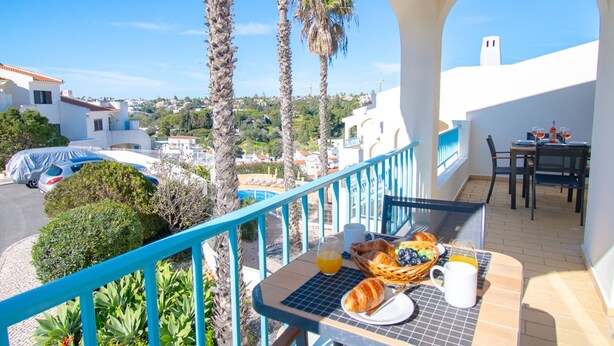 A balcony with breakfast setup, palm trees, and a view of the town. - 99B Hibiscus Monte Dourado (Lagoa)