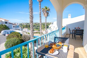 A balcony with breakfast setup, palm trees, and a view of the town. - 99B Hibiscus Monte Dourado (Lagoa)