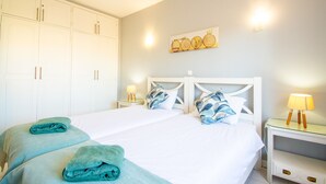 A hotel room with a large bed, white headboard, two bedside tables with lamps, and a wardrobe. - 99B Hibiscus Monte Dourado (Lagoa)
