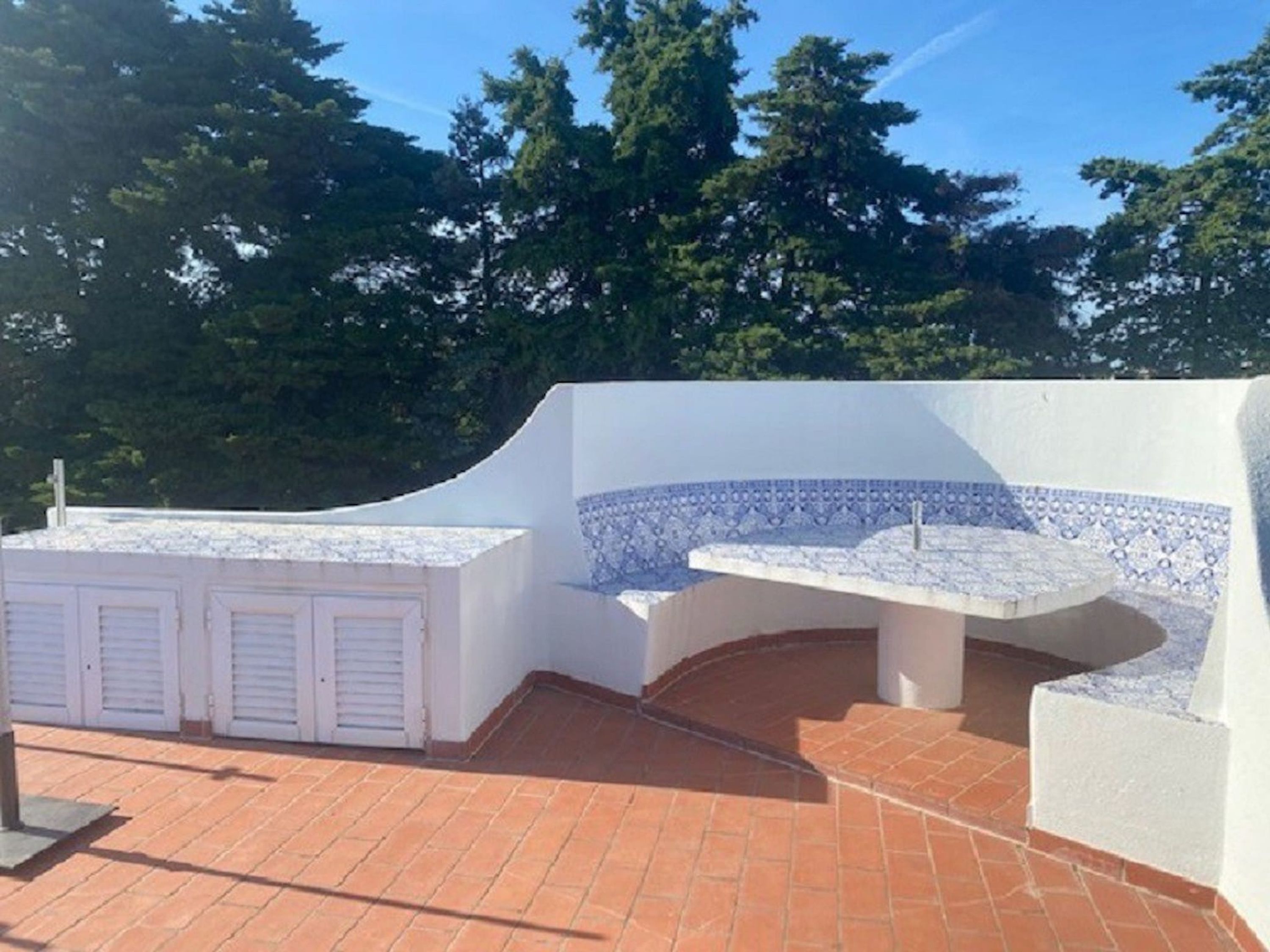 Une terrasse sur le toit, avec un mur blanc et un banc recouvert de carreaux bleus, entourée d’arbres.