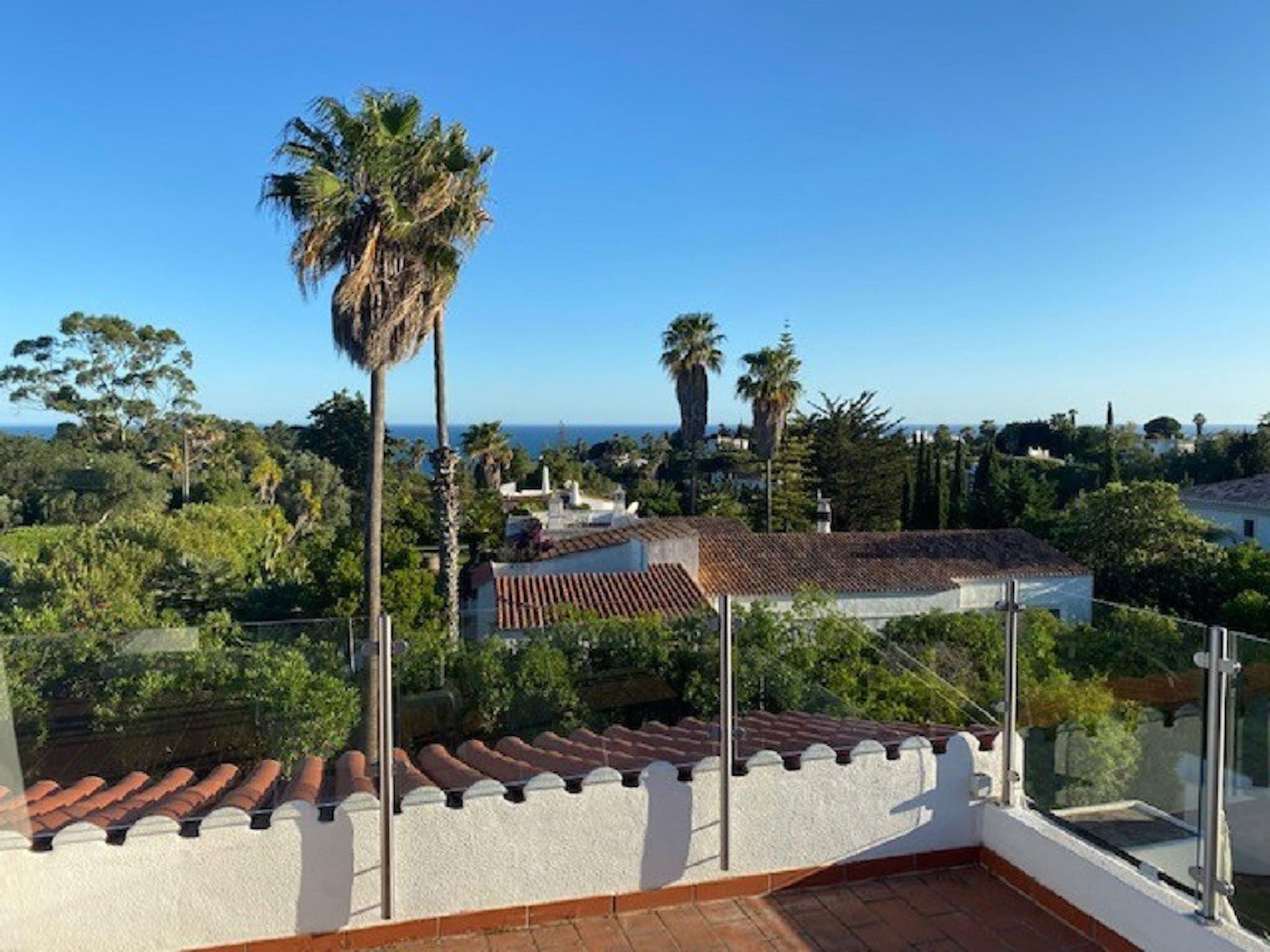 A rooftop terrace with a clear view of the surrounding landscape, including trees and a distant view of the sea.