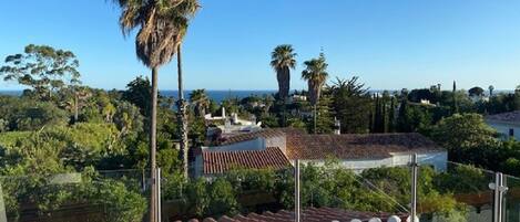 A rooftop terrace with a clear view of the surrounding landscape, including trees and a distant view of the sea.
