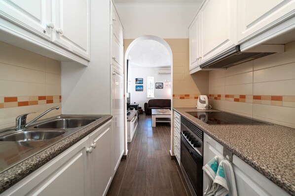 A narrow kitchen with white cabinets, a granite countertop, and a view into a living area. - C22 Quinta do Paraiso Superbly Appointed AND FUR (Lagoa)