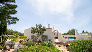A white building with a patio area, surrounded by various plants and a sandy ground. - 67 adm 3 Bedroom Villa Walking Distance to Carvo (Lagoa)
