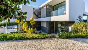 A modern two-story house with a stone facade, large windows, and a paved driveway.