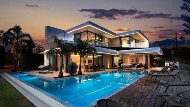 A modern two-story house with a swimming pool, outdoor seating, and a well-lit patio area.