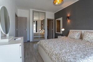 A modern bedroom with a large bed, a bedside table, a mirror, and a wardrobe.