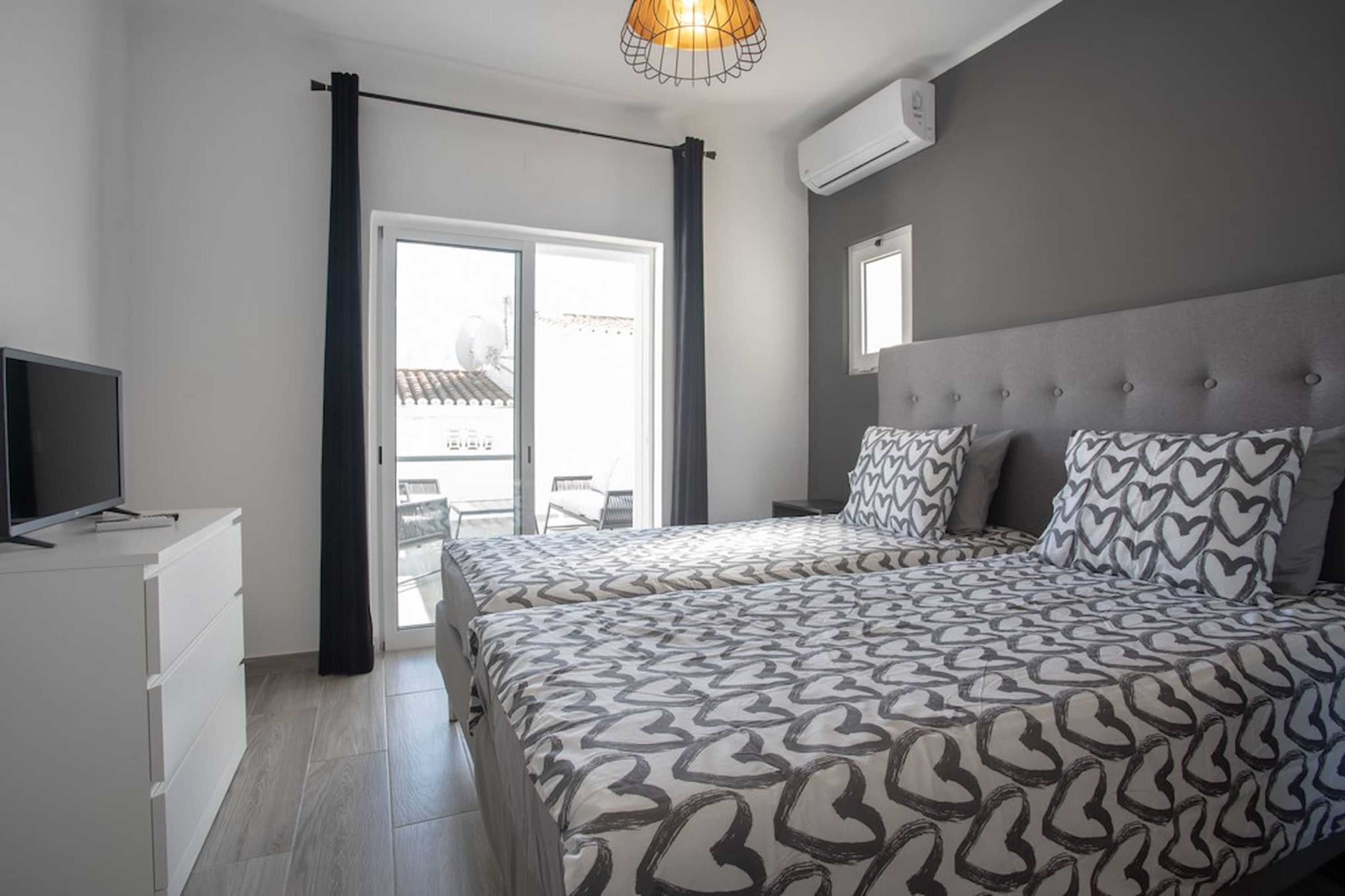Ein Schlafzimmer mit Bett, Fernseher, Schminktisch und einem Fenster mit Vorhängen.
