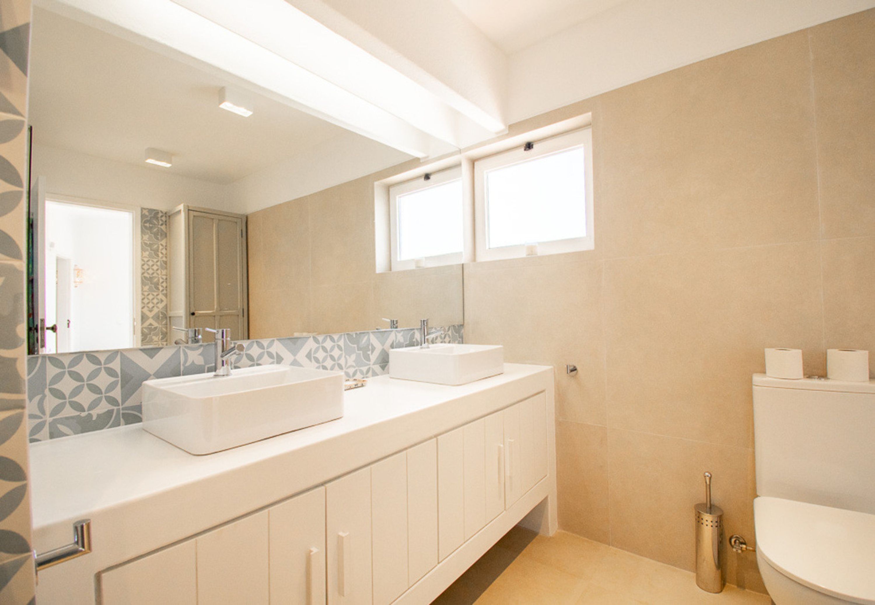 A modern bathroom with two sinks, a large mirror, and a toilet.