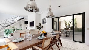 Un'area pranzo moderna con un tavolo in legno, sedie e lampade a sospensione. Si nota una scala sullo sfondo che conduce a un piano superiore.