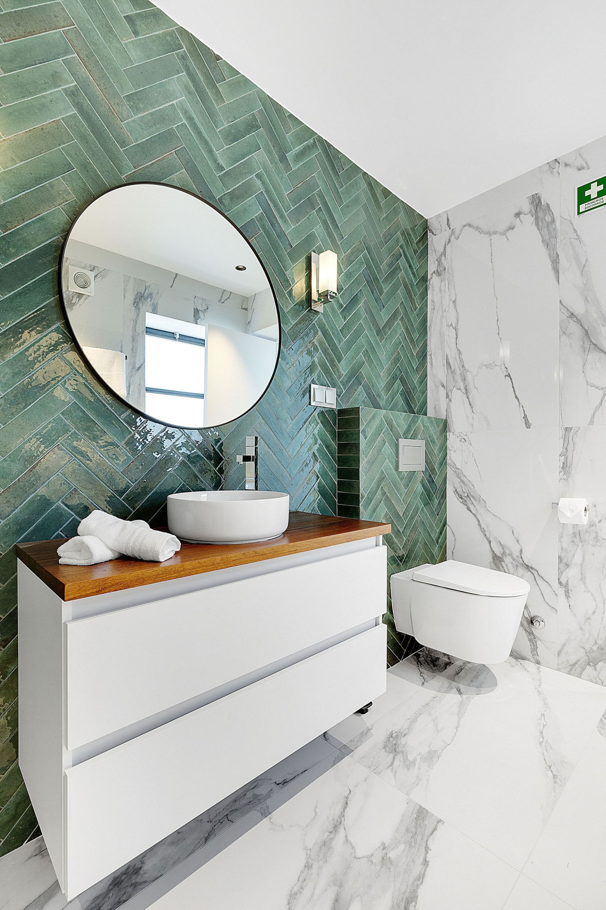 Een moderne badkamer met een backsplash van visgraat tegels, een ronde spiegel, een wastafel en een toilet.