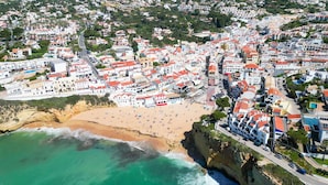 Vista aerea di una cittadina costiera con spiaggia, edifici bianchi a tetti rossi e una limpida visione dell'oceano.