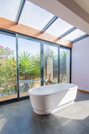 A modern bathroom with a freestanding bathtub, large windows, and a view of greenery outside. - Yoba Horse Farm in Carvoeiro (Lagoa)
