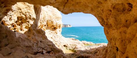 A natural cave opening with a view of the sea and a distant cliff.