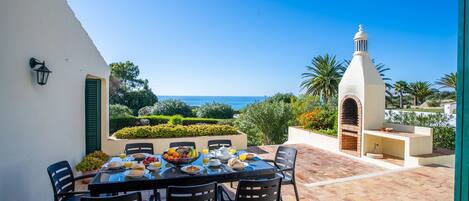 A patio with a table set for breakfast, overlooking a scenic view of the sea and a white building with a tower.