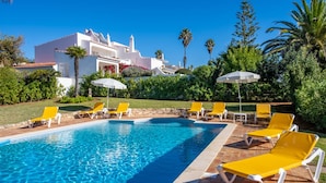 A swimming pool with yellow lounge chairs and umbrellas, surrounded by greenery and a white building with a red-tiled roof. - 7 Club Atl Ntico Fabulous Five Bedroom Villa WI (Lagoa)