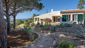 A Mediterranean-style villa with a gravel driveway, surrounded by a variety of plants and trees, and a view of the sea. - 7 Club Atl Ntico Fabulous Five Bedroom Villa WI (Lagoa)