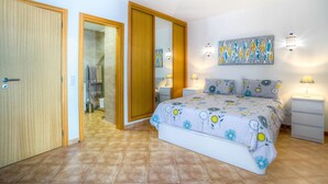 A bedroom with a bed, bedside tables, a nightstand, a painting, and a bathroom visible through an open door. - Elizabet Modern Apartment in the Heart of the Ci (Lagoa)