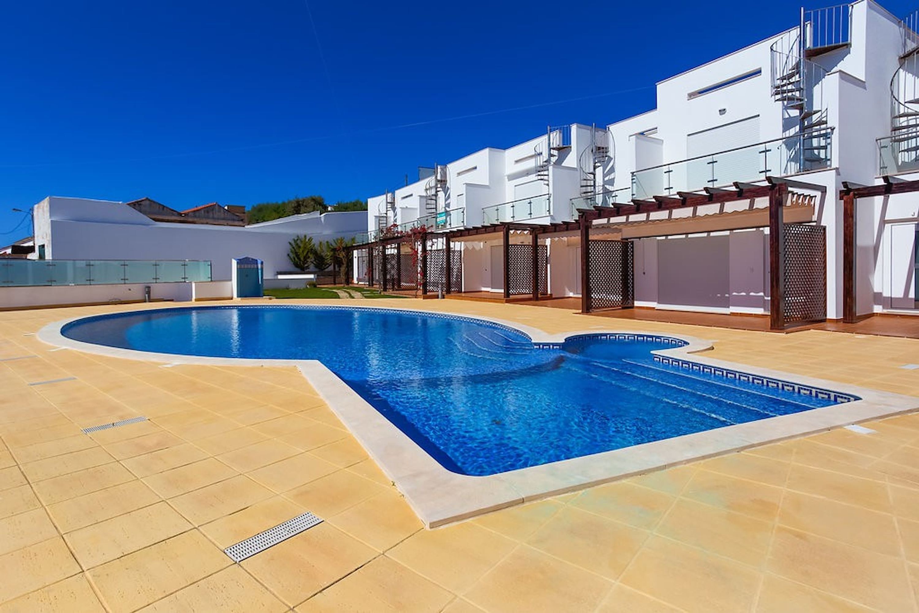 A swimming pool with a curved design, surrounded by a tiled deck.
