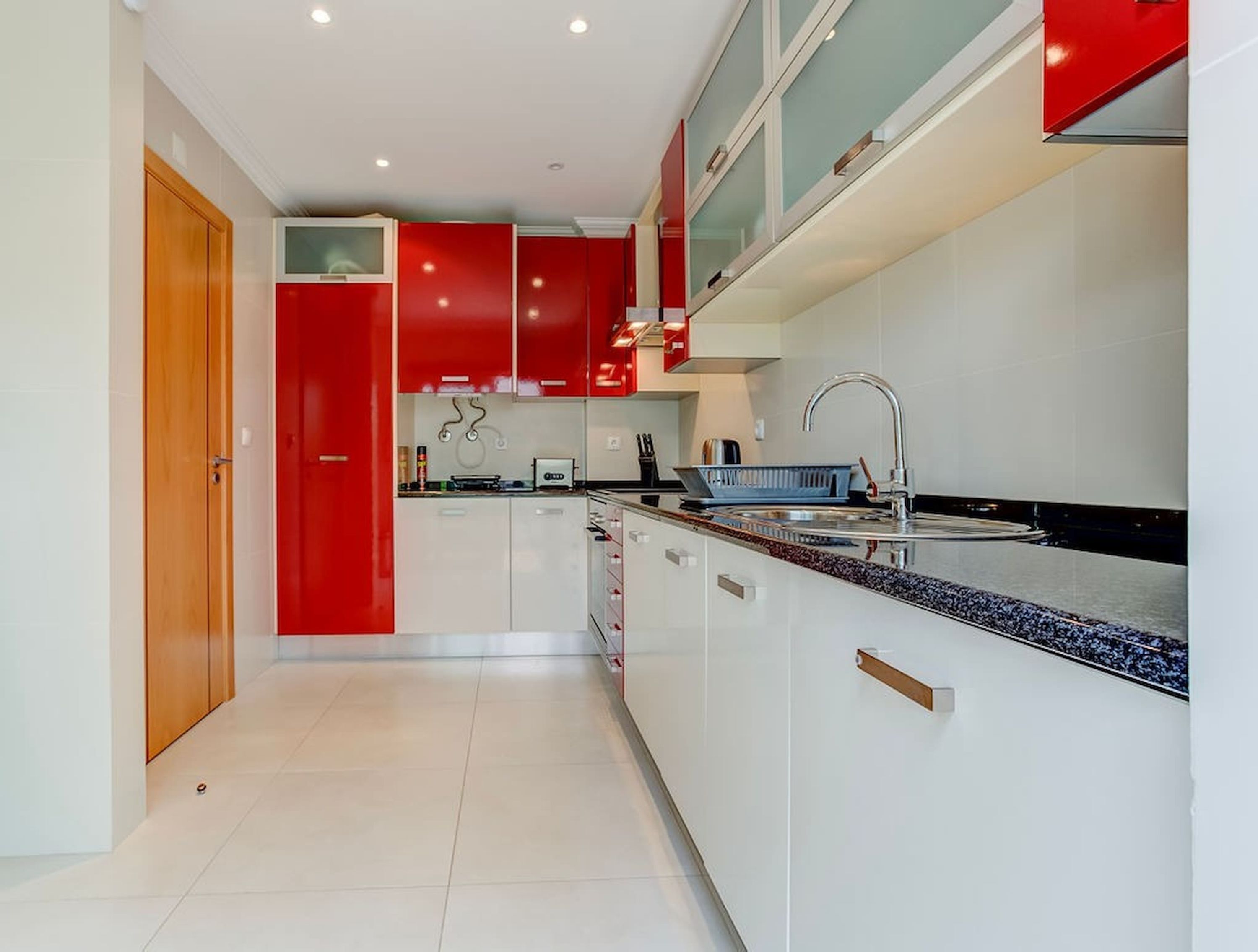 A modern kitchen with white cabinets, red accents, and a granite countertop.