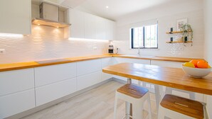 A modern kitchen with white cabinets, a wooden countertop, and a window providing natural light. - Casa Mel in Carvoeiro (Lagoa)