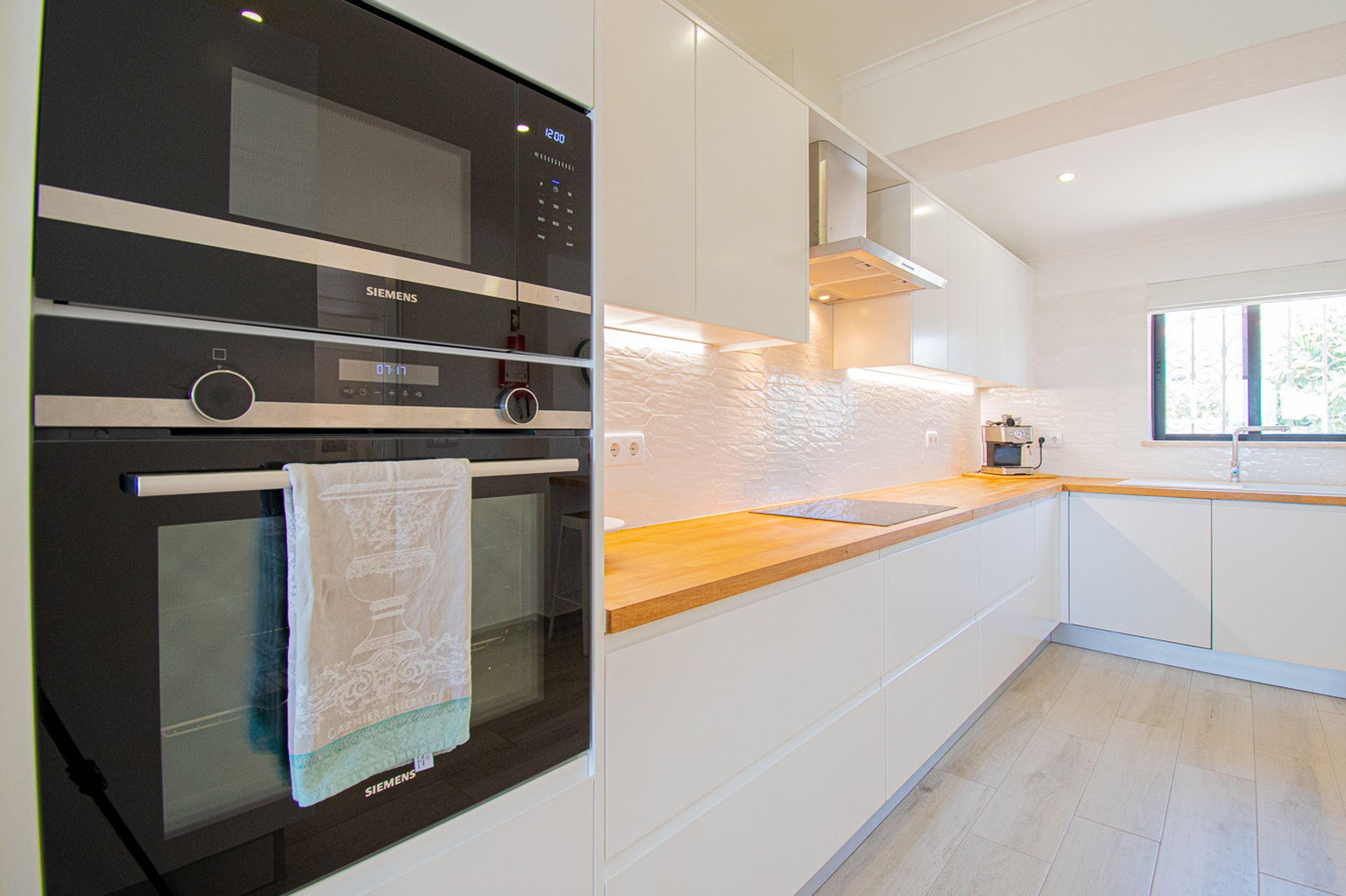 A modern kitchen with white cabinetry, a wooden countertop, and a Siemens oven.