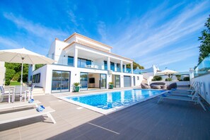 A modern house with a swimming pool, outdoor seating, and a large glass door entrance. - Ilha do Sol Luxury in an Ideal Location (Lagoa)