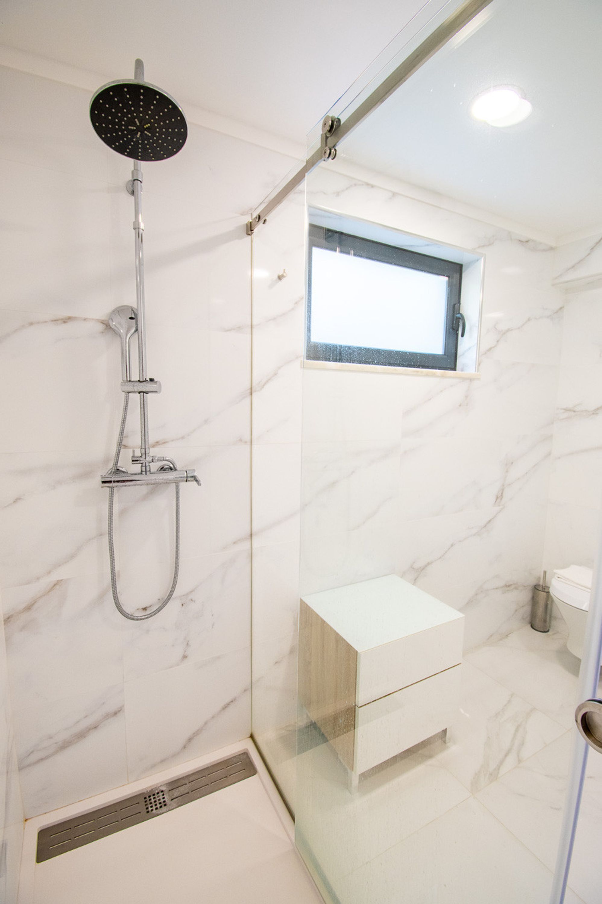 A modern bathroom with a glass-enclosed shower, a small window, and a minimalist vanity.
