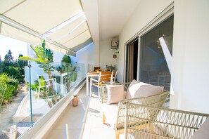 Ein Balkon mit Glastrennwand, Korbmöbeln und einem Tisch mit Stühlen.