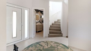 A hallway with a staircase, a round rug, and a door with a mirror. - Casa Ella - Beautifully Renovated Townhouse Walkin (Lagoa)