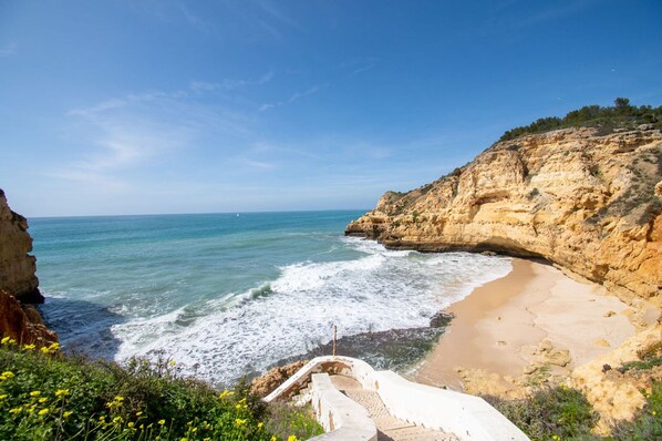 A coastal landscape with a beach, rocky cliffs, and a clear sky.