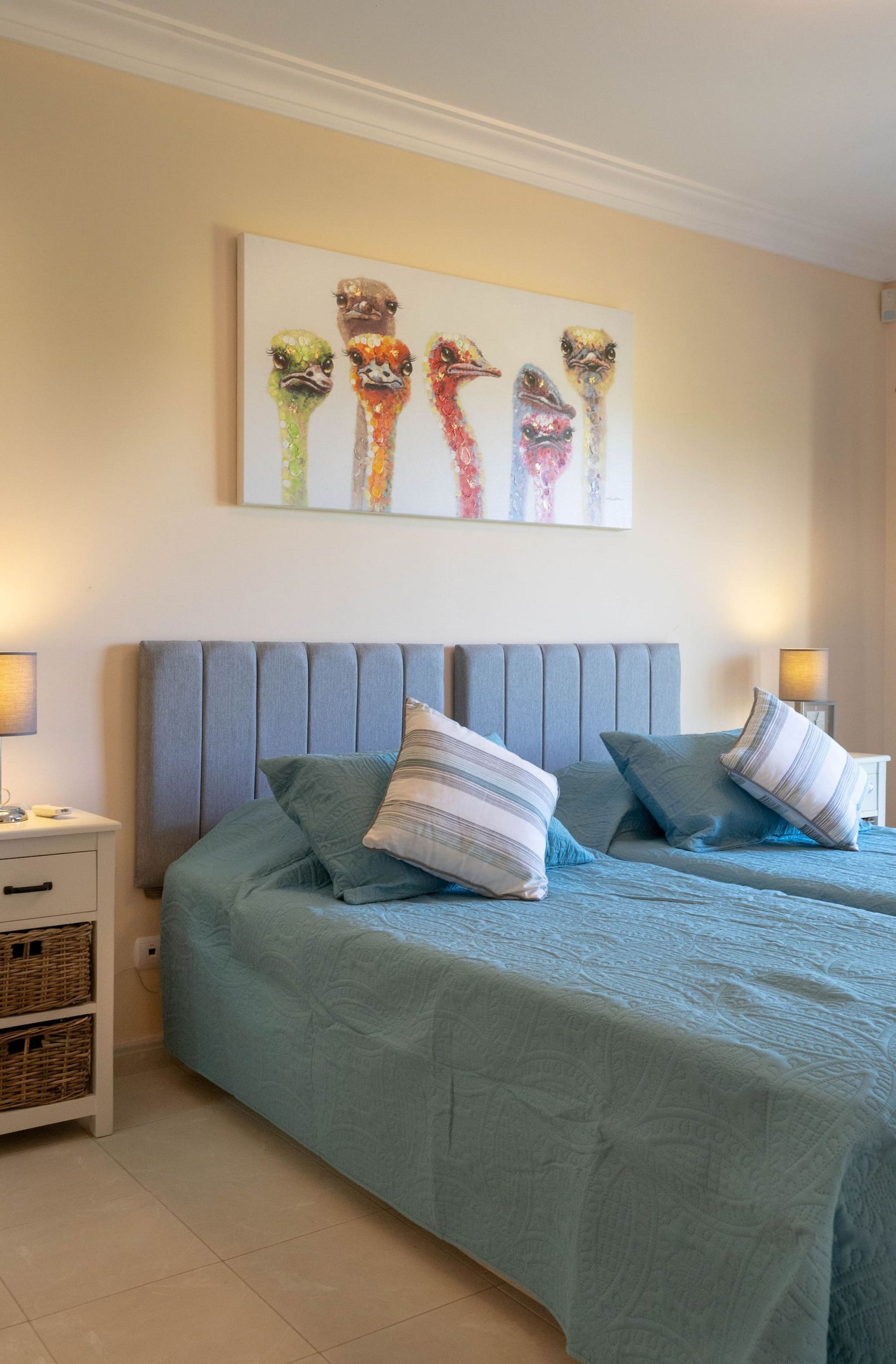 A bedroom with a bed, pillows, a bedside table, a lamp, and a wall art piece.