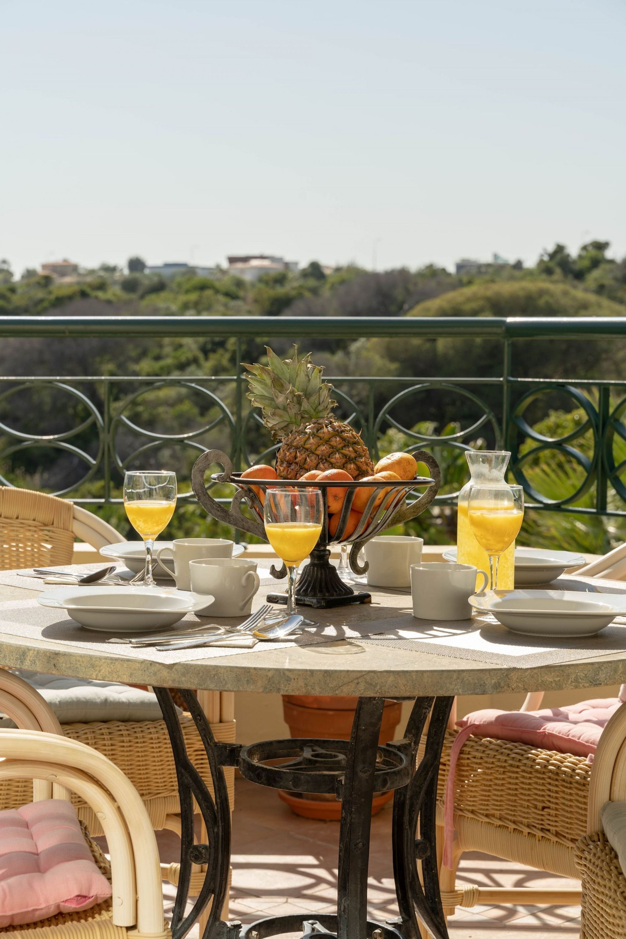 A round table with a pineapple centerpiece, surrounded by wicker chairs and a metal railing.