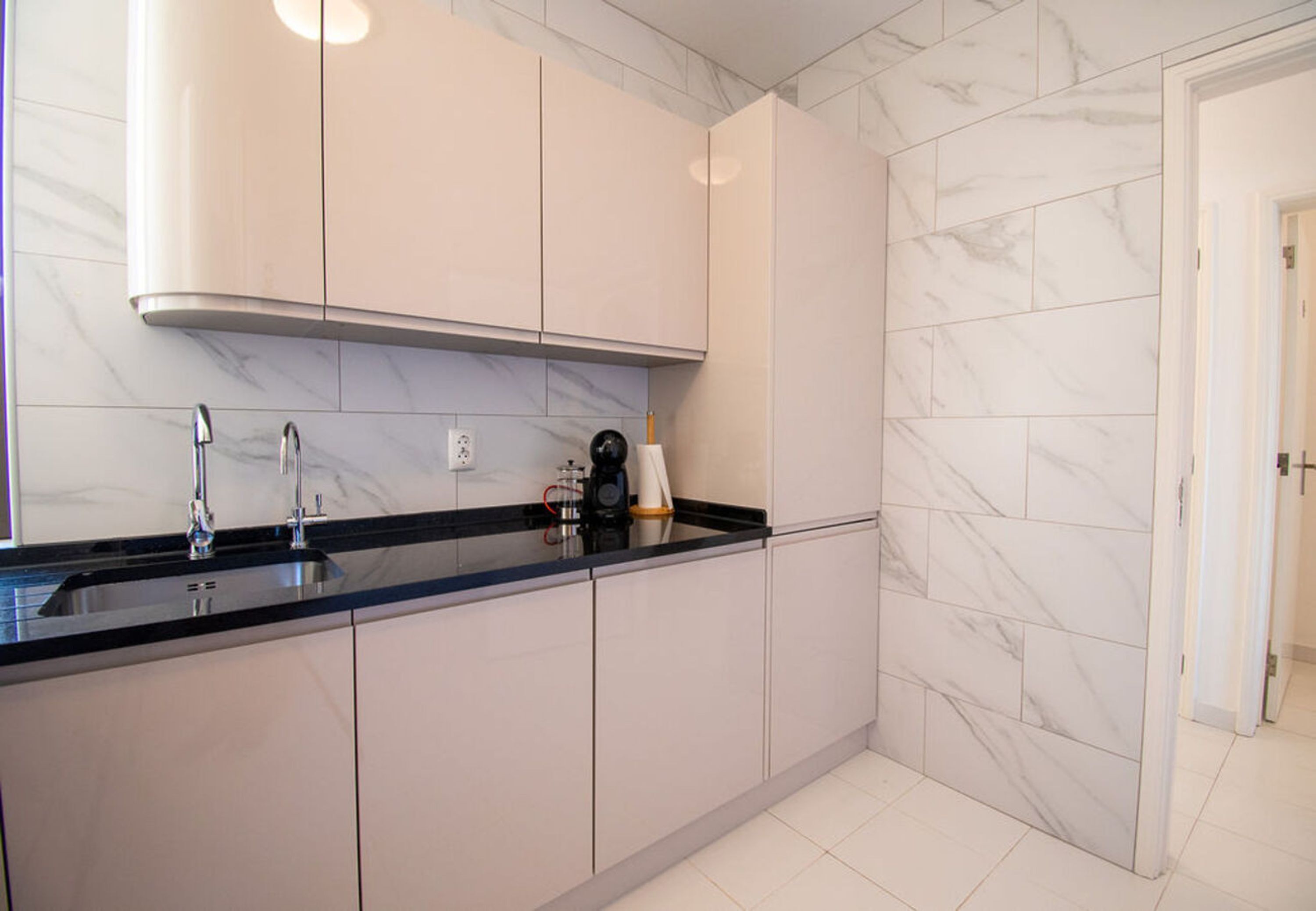 A modern kitchen with a black countertop, stainless steel sink, and marble backsplash.