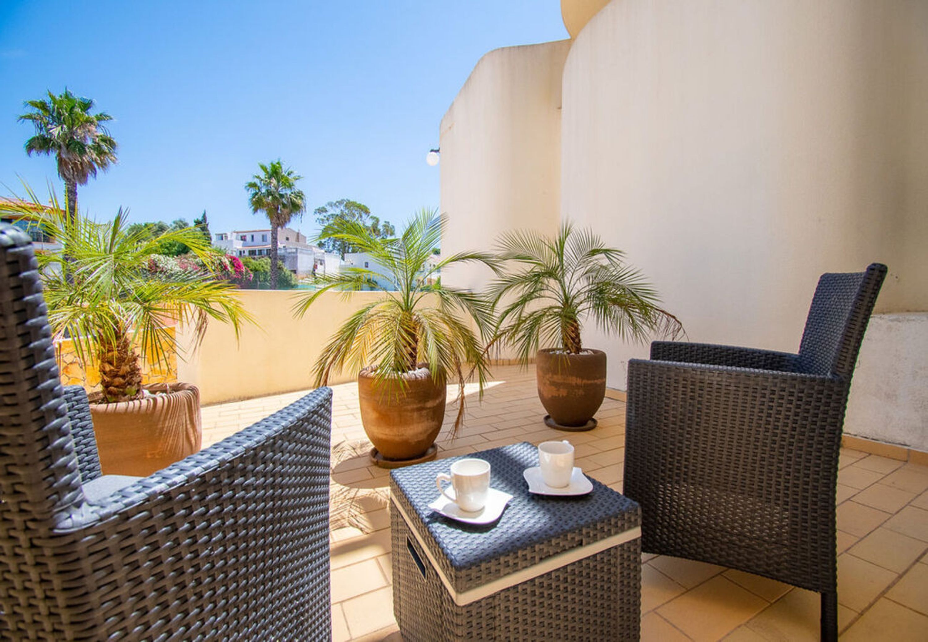 An outdoor seating area with wicker furniture, potted plants, and a view of buildings in the background.
