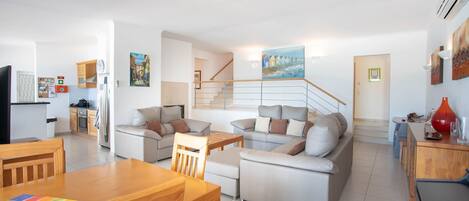 A modern apartment with a living room, dining area, kitchen, and a staircase leading to an upper floor.
