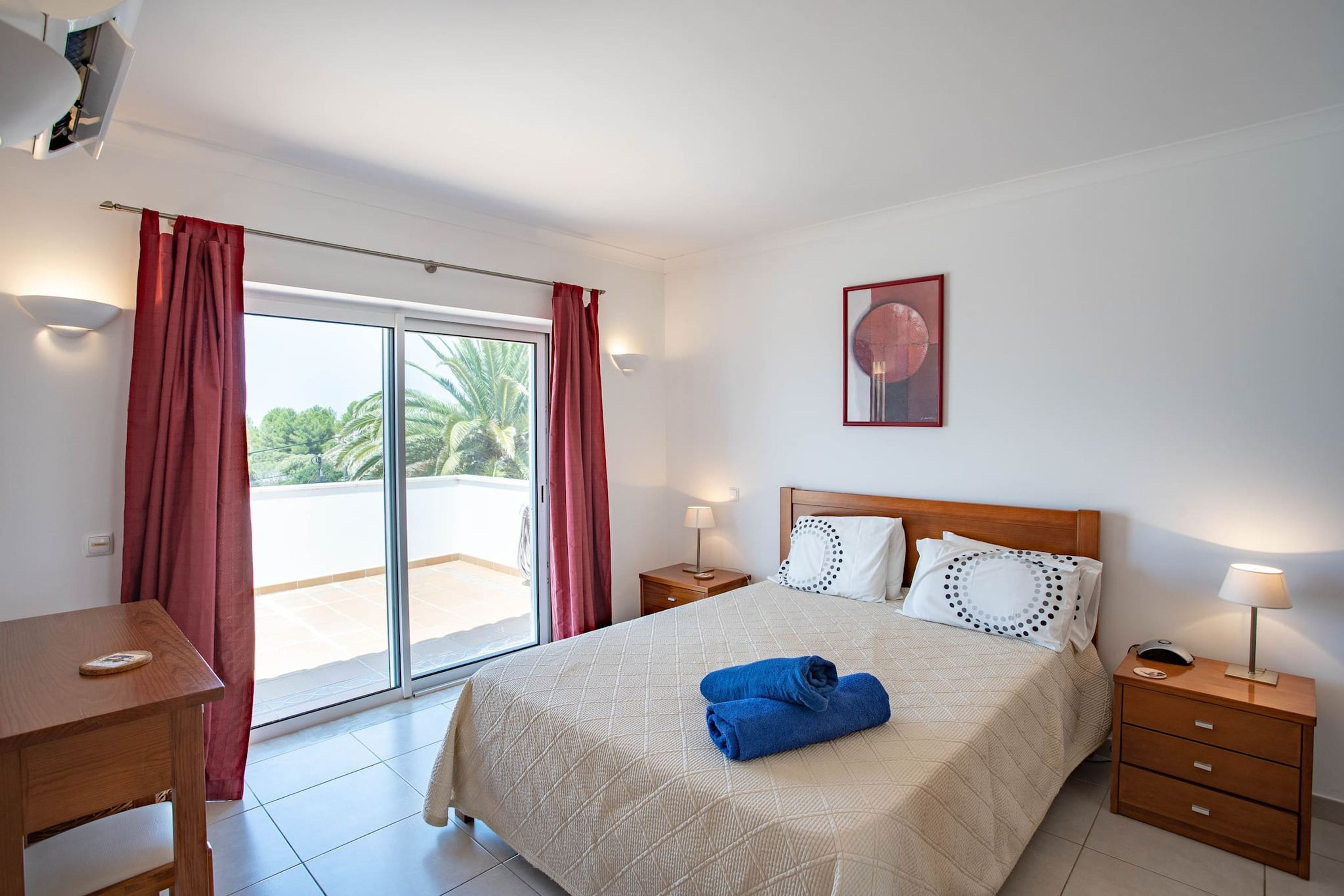 Een hotelkamer met een bed, een bureau, een nachtkastje en een raam met gordijnen.
