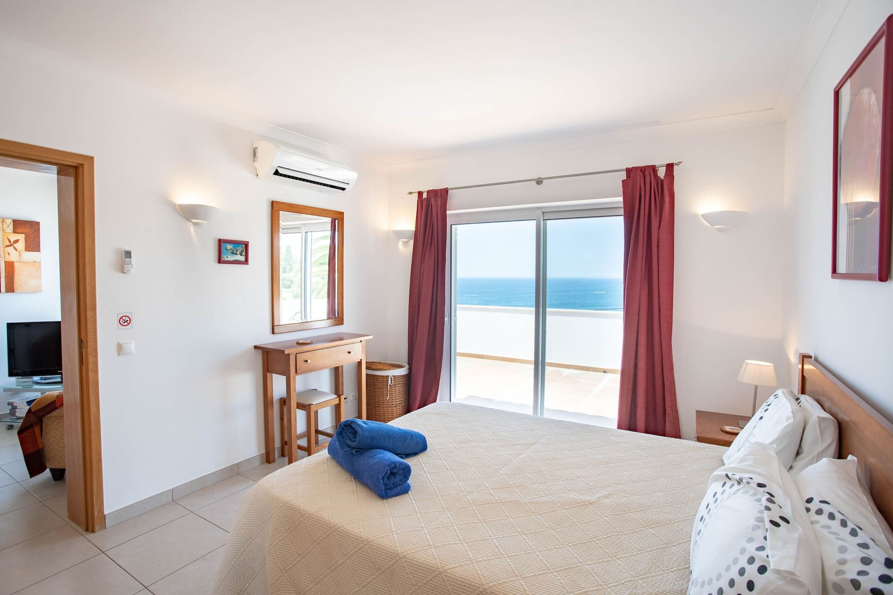 A hotel room with a bed, a desk, a chair, a TV, and a view of the sea.