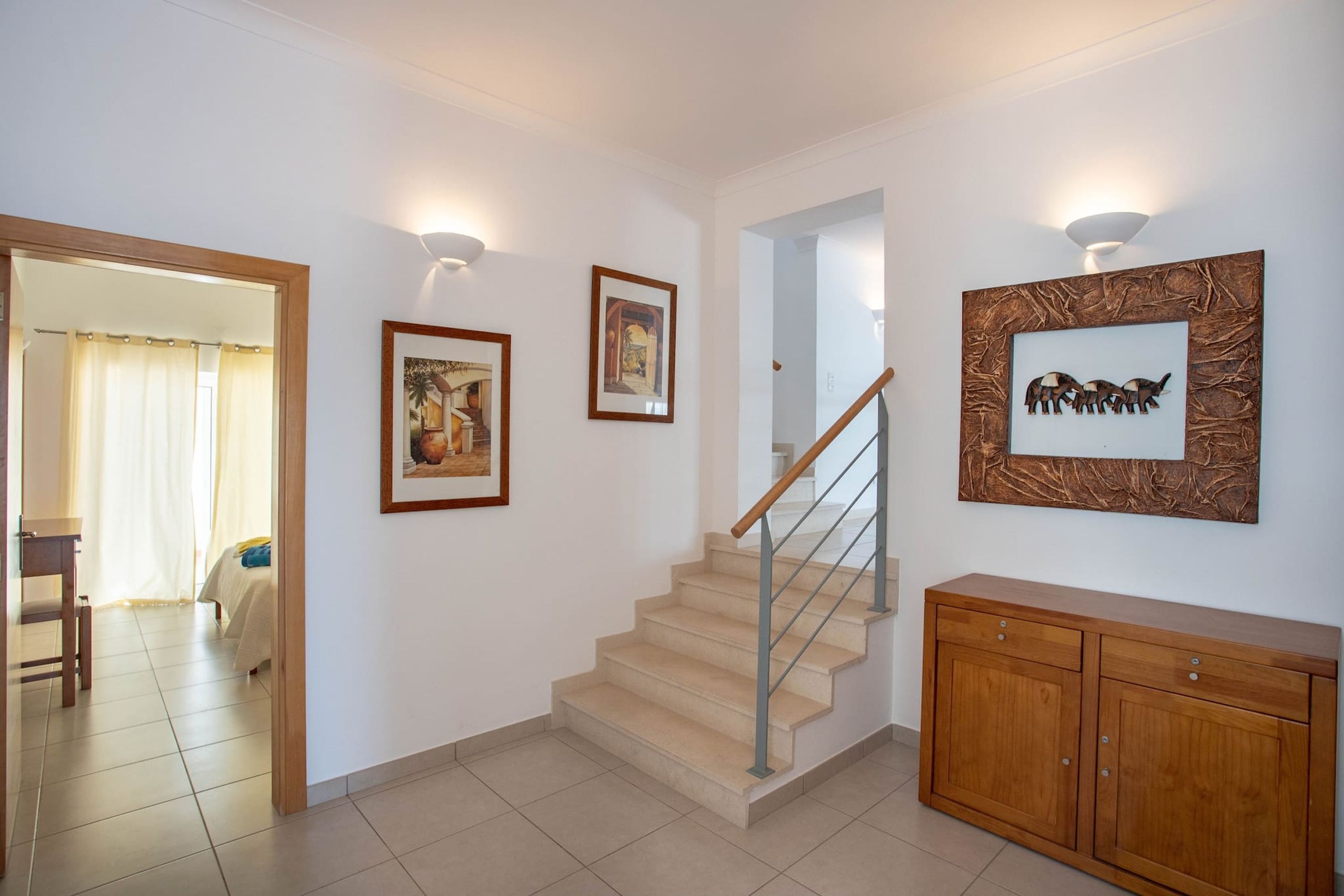 A staircase with a wooden handrail, a wooden cabinet, and three framed pictures on the walls.