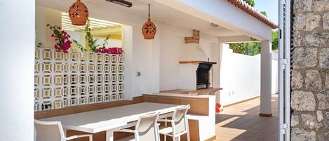 An outdoor patio with a white table and chairs, a decorative wall with geometric patterns, hanging terracotta lanterns, and a stone wall.
